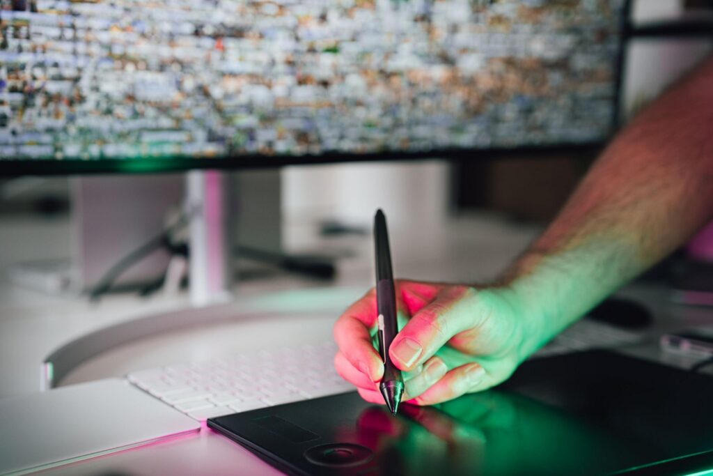 Graphiste utilisant un stylet sur une tablette graphique devant un écran d'ordinateur, création graphique par une agence spécialisée en design