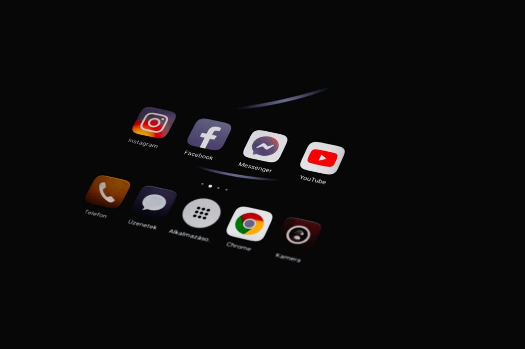 Écran de smartphone affichant les icônes des réseaux sociaux Instagram, Facebook, Messenger et YouTube pour une agence de communication digitale