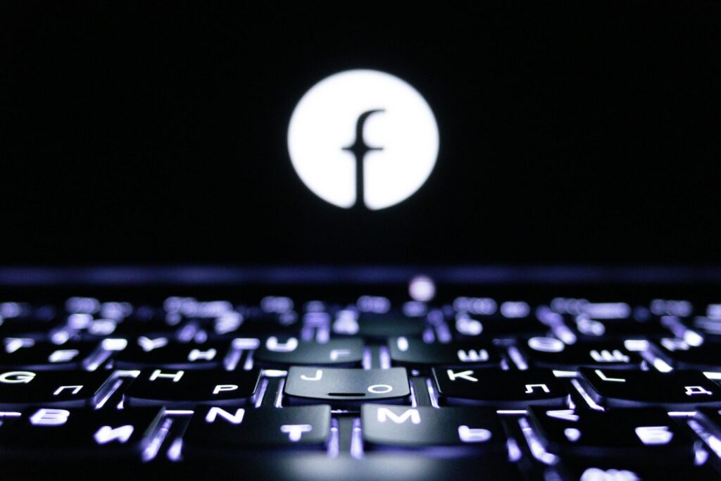 Logo Facebook illuminé sur écran d'ordinateur avec clavier rétroéclairé pour la gestion de campagnes publicitaires Facebook Ads
