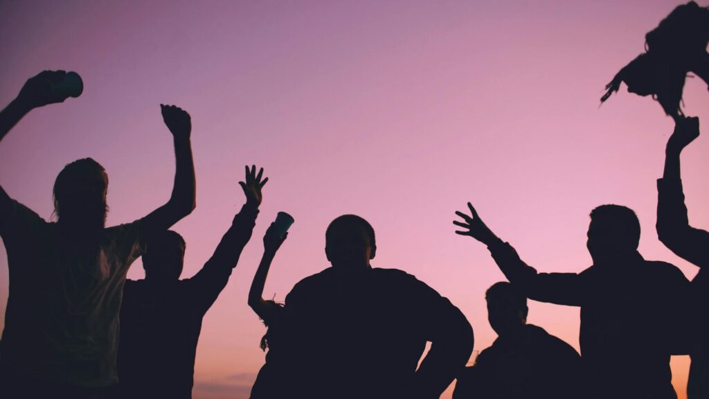 Silhouettes de personnes les bras levés lors d'un événement au coucher de soleil, communication événementielle par une agence spécialisée